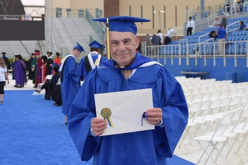 man holding recognition certificate wearing academic regalia